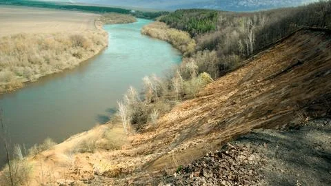 River flows beneath steep bank in natural landscape near forest during dayt.. Fotos de archivo