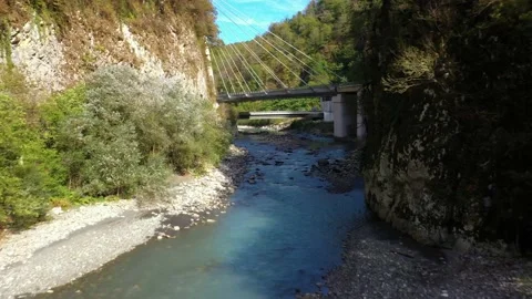 River flows between rocky banks under suspension bridge Video stock 150828502