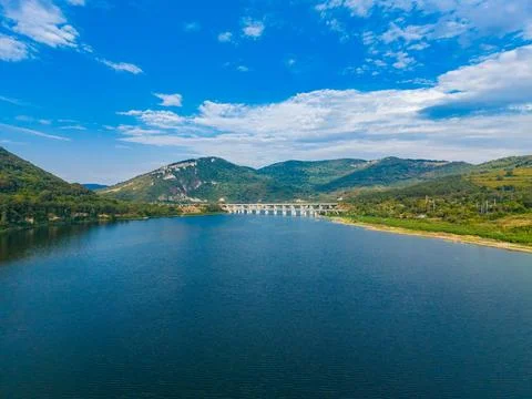 A river flows calmly with green mountains on either side. A bridge spans the  Stock-Fotos