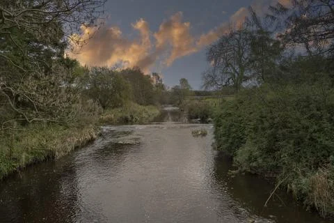 River flows gently through lush green banks Stock Photos