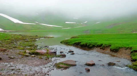 River flows from Lake in at green hill in High Snowy Mountains with Clouds 스톡 동영상 65763534