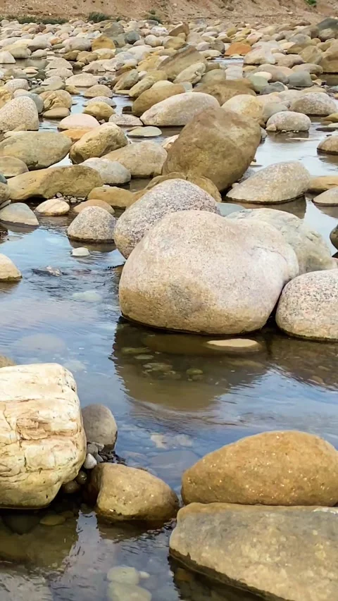 A river flows over rocks in a natural setting surrounded by hills under clear 스톡 동영상 330989996