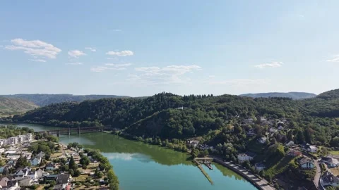 A river flows past hillside homes and a bridge beneath wooded slopes 動画素材 342336712