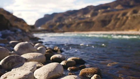 A river flows with rocks by the shore, mountains in the background Stock Footage 271479693