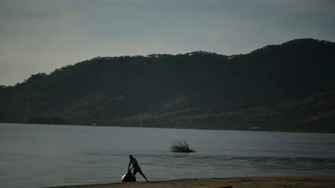 The River Flows Slowly, Mountains Stand Tall, a Fisherman Is Pushing His Boat Stock Footage 306715272