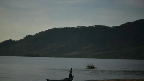 The River Flows Slowly, Mountains Stand Tall, a Fisherman Is Pushing His Boat Stock Footage 306715274
