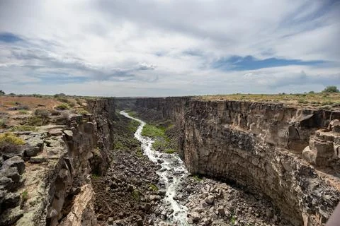 A river flows through a canyon with a cloudy sky in the background Stock Photos