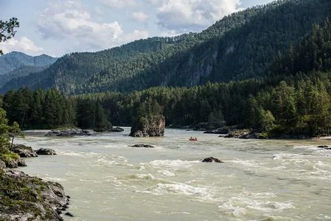 A river flows through a lush forest with mountains in the background Stock Photos