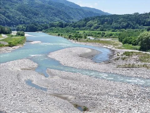 River flows through rocky bed, winding through green hills Stock Photos