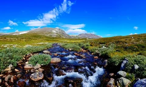 River flows through rocky landscape under blue sky with clouds Stock Photos