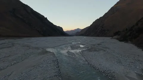 River flows through rocky valley at dusk, camera pans across the landscape Video stock 320395386