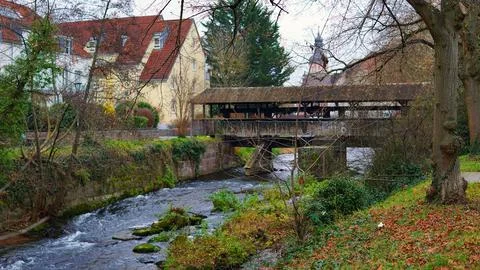 A river flows through which an old wooden bridge with a roof passes Stock Photos