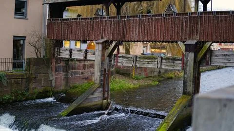 A river flows through which an old wooden bridge with a roof passes. The bridge Stock Photos