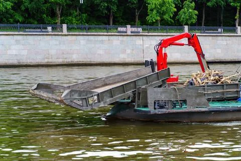 A river garbage collection ship sails down a river with a raised bucket Stock Photos
