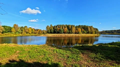 River gently flowing past a forested bank showcasing autumn colors under a Stock-Footage 330991864