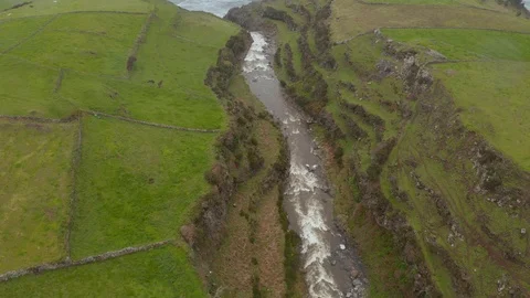 River in gorge between green fields falls as waterfall into the sea. Aerial of Stock Footage 117770248