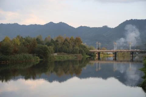 A river with green trees on both sides, reflecting the distant mountains an.. Stock Photos