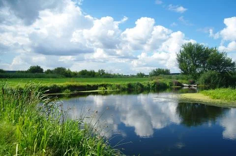 River, land with trees and cloudy sky Stock Photos