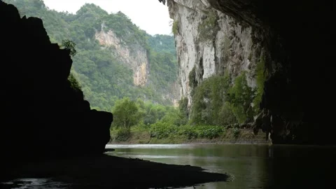 A river lined with forest and cliffs filmed from inside a dark cave, in Vietnam Stock Footage 232431359
