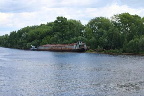 River with lonely rusty cargo ship dire straits among bushes and trees Stock Photos