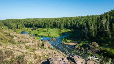 A river meanders through a verdant forest under a clear blue sky Foto stock