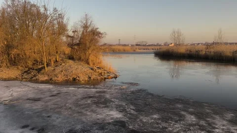 River with melting ice and bare trees under warm evening light, 스톡 동영상 344549613