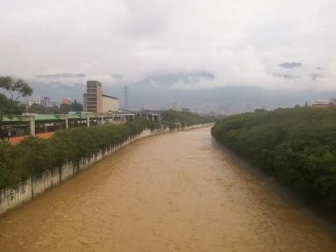River of muddy brown water flowing through a city on a cloudy day Stock Photos