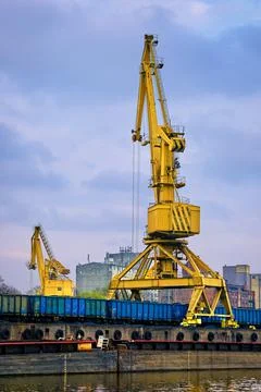 River port crane loading open-top gondola cars on cloudy day. Empty river drag Stock Photos
