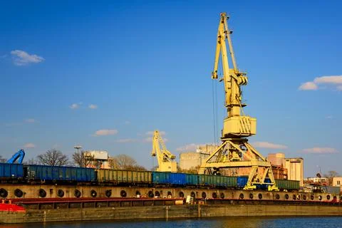 River port crane loading open-top gondola cars on sunny day. Empty river drag Stock Photos