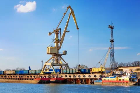 River port crane loading open-top gondola cars on sunny day. Empty river drag Stock Photos