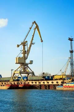 River port crane loading open-top gondola cars on sunny day. Empty river drag Stock Photos