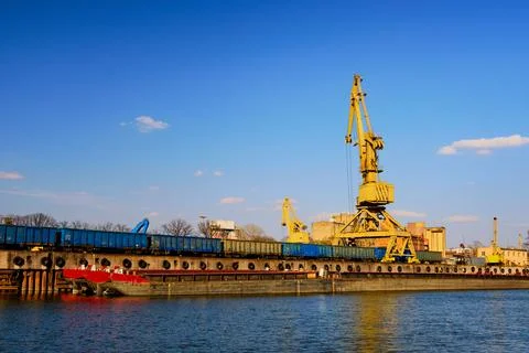 River port crane loading open-top gondola cars on sunny day. Empty river drag Stock Photos