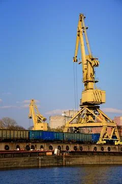 River port crane loading open-top gondola cars on sunny day. Empty river drag Stock Photos