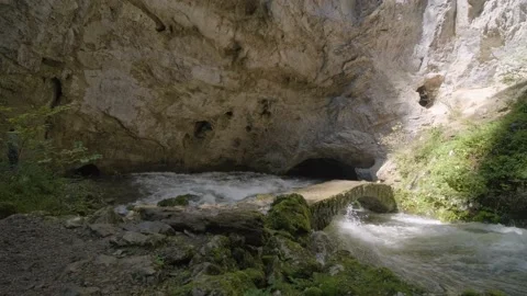 River Rak Flows Under Old Natural Stone Bridge With Cave in Background. Stockbeeldmateriaal 142968608
