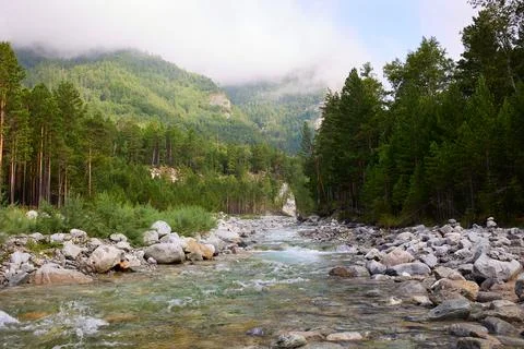 A river with a rapid current, mountain peaks in the clouds Stock Photos