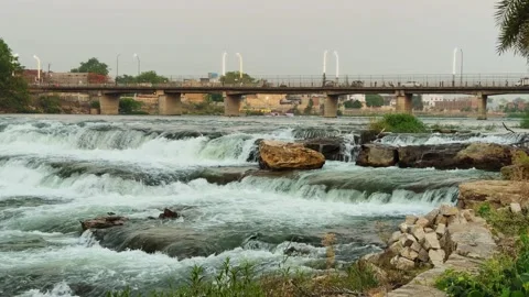 River Rapids Flowing Over Rocks with Bridge Background Stock Footage 334173407