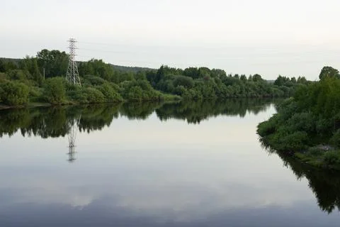 River with reflected clouds, forest on the banks and power tower Stock Photos