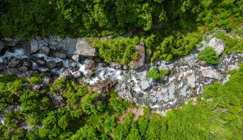 River running down the mountain by rocks and trees. Aerial Nature Foto stock