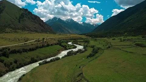 River running through a lush green valley surrounded by mountains and a lush Stock Footage 243875801