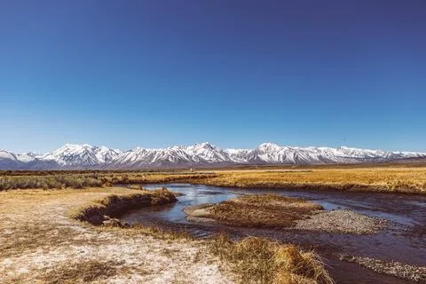 River runs though Arid plain against Sierra Nevada Mountains blue sky 写真素材