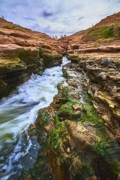River Rushing Through Red Rock Canyon and Mossy Cliffs Under Dramatic Sky Stock Photos