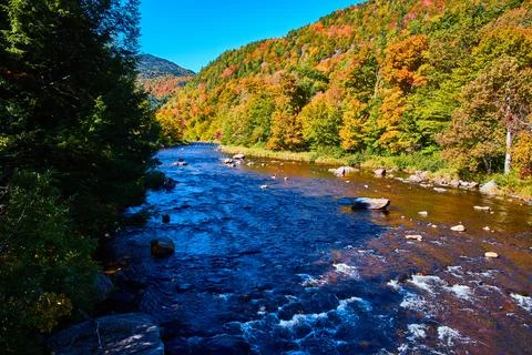 River with small rapids in shade along sunny hills of fall foliage Foto stock