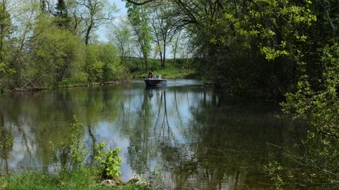 River with trees along the shore and a slowly approaching motor boat. Stock Footage 201306522