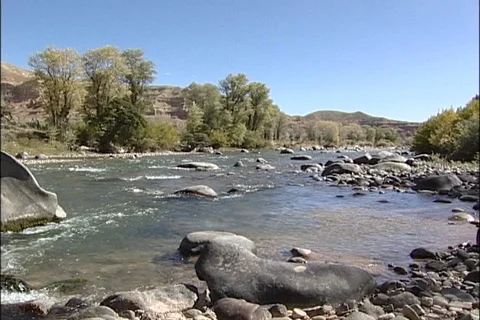 River Tumbling through Rocks past Treed Riverbank Video stock 121334195