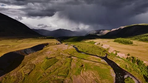 The river valley meanders through summer fields with thunderous mountains and Stock Footage 332659685