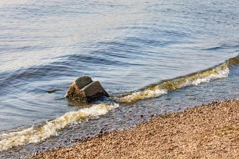 A river wave rolls over a coastal boulder on a sunny day. Stock Photos
