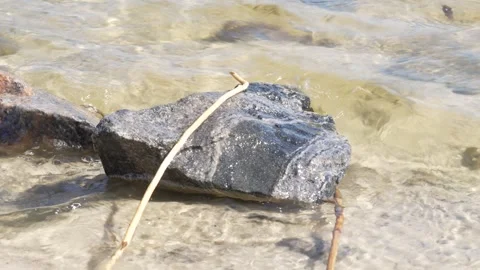 River waves washing over a dark stone on the shore Vídeos de archivo 334451582