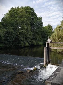 River weir with leafy green trees and mellow sky Stock Photos