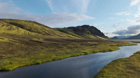 River winding through mossy plains and rugged hills under a streaked sky Stock Footage 325187295