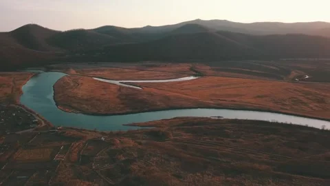 River winding through valley with mountains, grassy slopes, and clear blue sky Stock Footage 274828052